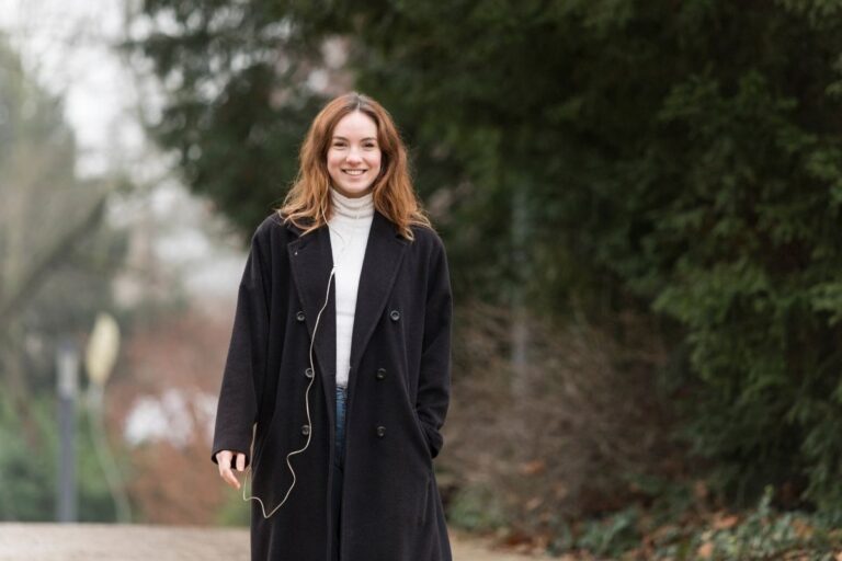 Young woman wearing wool coat in park smiling.